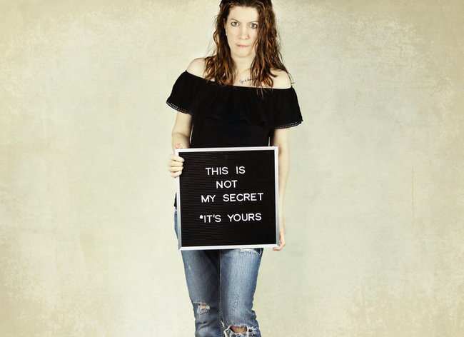 Person holding a sign reading 'This is not my secret, it's yours'